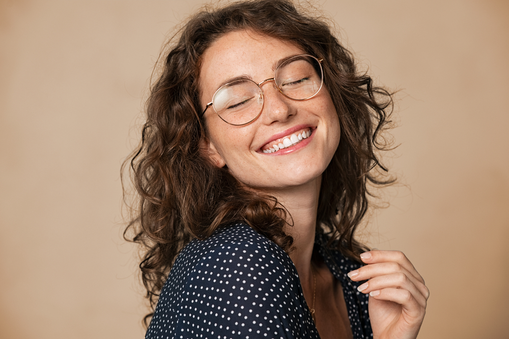 Casual cheerful woman with eyeglasses smiling a camera on cream background - Dental Implants in Seattle