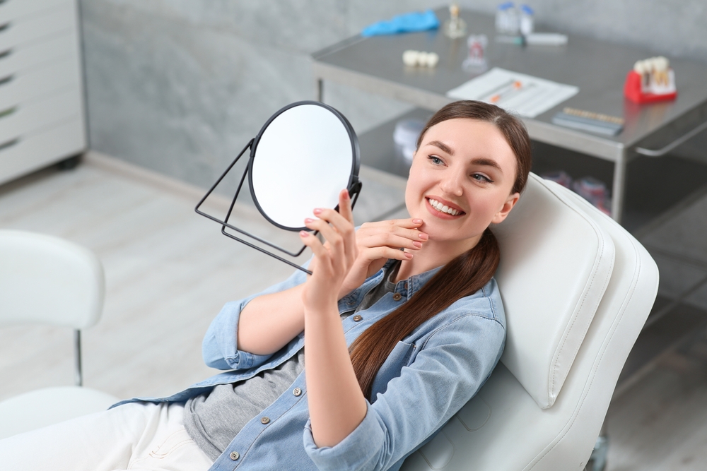 Woman checking her teeth on a mirror - Dental Crown in Seattle